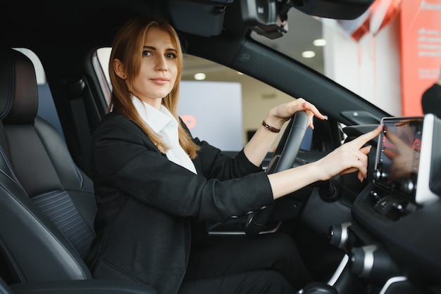 Young beautiful woman showing her love to a car in a car showroom