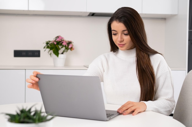 Young beautiful woman sits at her workplace and open the laptop for working online