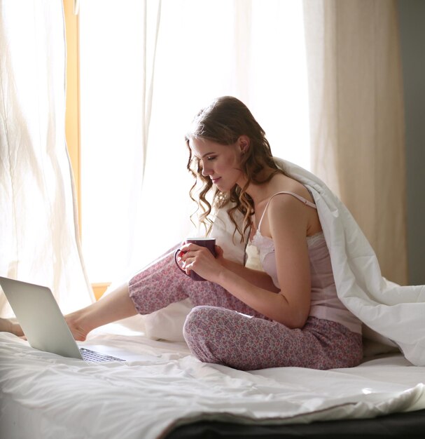 Young beautiful woman sitting in bed with laptop