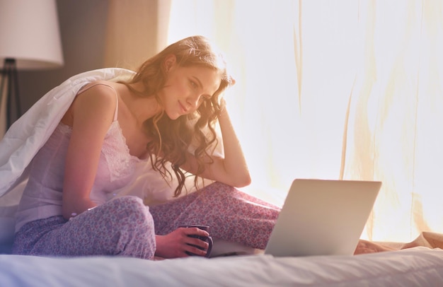 Young beautiful woman sitting in bed with laptop