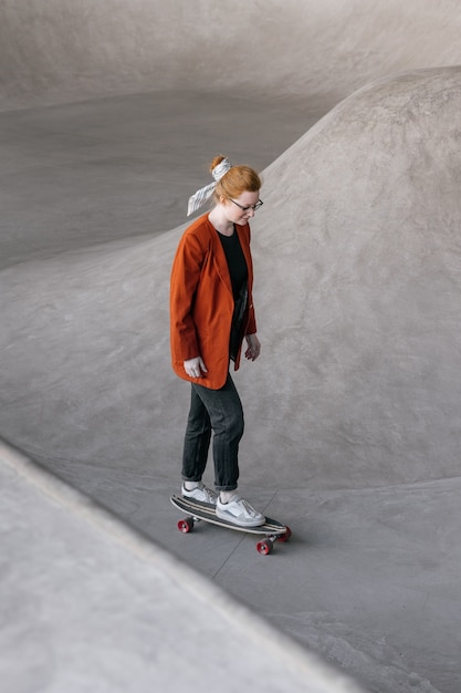 A young and beautiful woman skater a woman in an orange jacket rides a skateboard on a skate pad