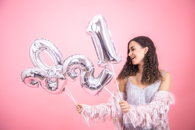 Young beautiful woman smiling on a pink wall with silver balloons for the new year concept