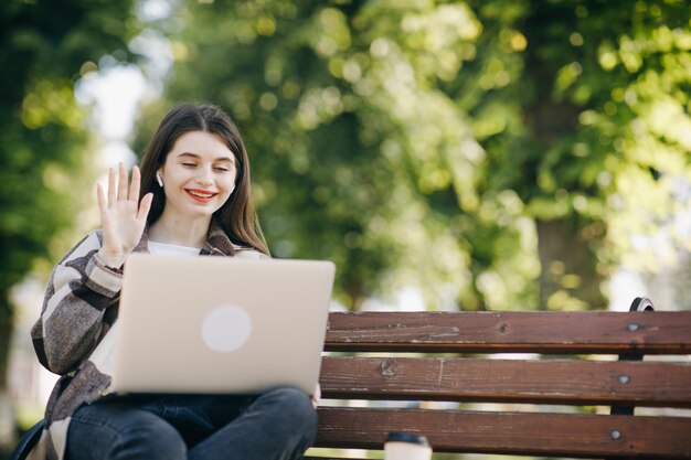 Young beautiful woman standing on a bench using the laptop