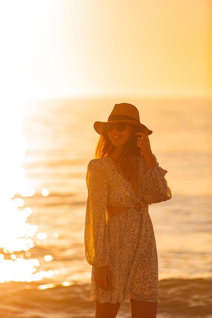 Young beautiful woman at straw hat on the beach at sunset