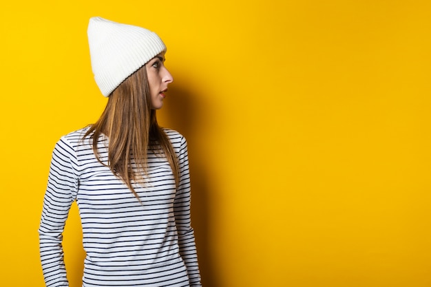 Photo young beautiful woman in a striped sweater and hat looks away on a yellow background