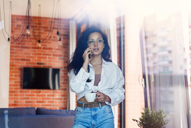 Young beautiful woman talking on smartphone solve business from home and hold cup of coffee or tea