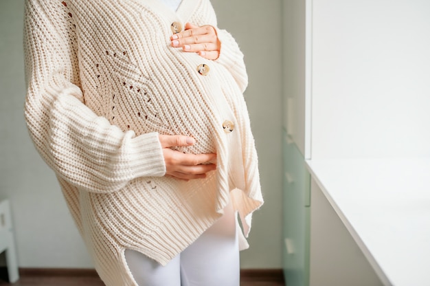 Young beautiful woman in the third trimester of pregnancy. Cropped shot of pregnant woman in knitted sweater with hands on belly