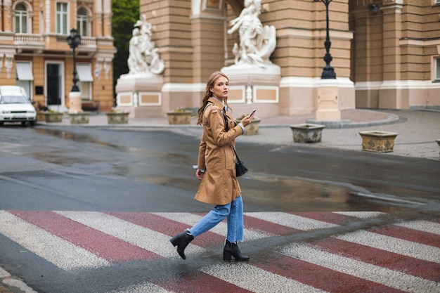 Young beautiful woman in trench coat and jeans thoughtfully 