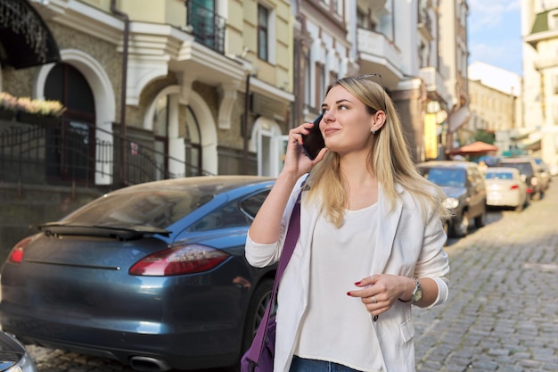 Young beautiful woman walking along city street talking on mobile phone