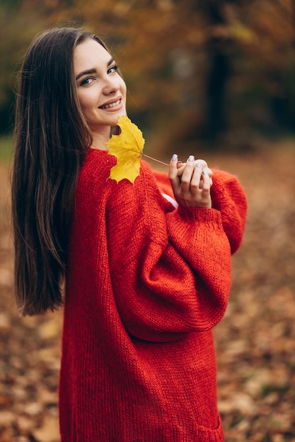 Young beautiful woman walking in autumn park and holding leaves