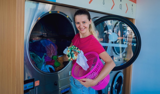 Young beautiful woman washes and dries clothes in the laundry