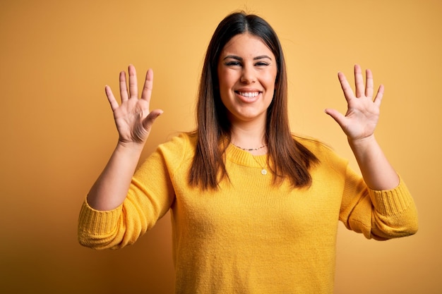 Young beautiful woman wearing casual sweater over yellow isolated background showing and pointing up with fingers number ten while smiling confident and happy