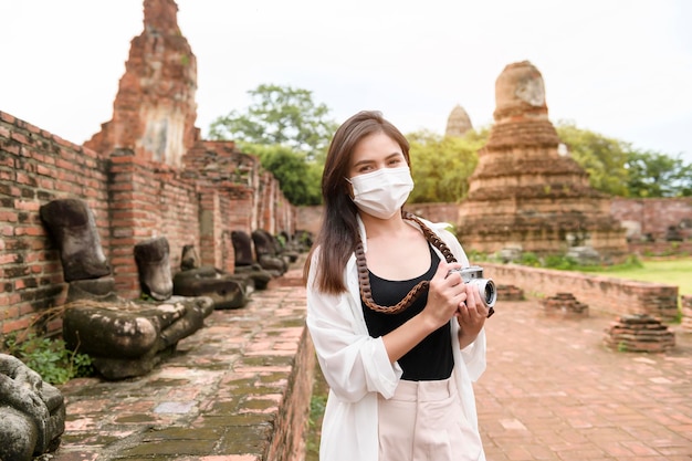 Young beautiful woman wearing protective mask traveling and taking photo at thai historical