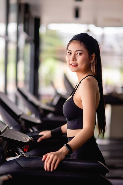 Young beautiful woman wearing sportswear, Sweat-proof fabric and smartwatch standing on treadmill warm up before run to workout in modern gym