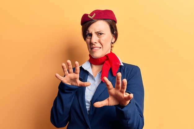 Young beautiful woman wearing stewardess uniform disgusted expression displeased and fearful doing disgust face because aversion reaction with hands raised