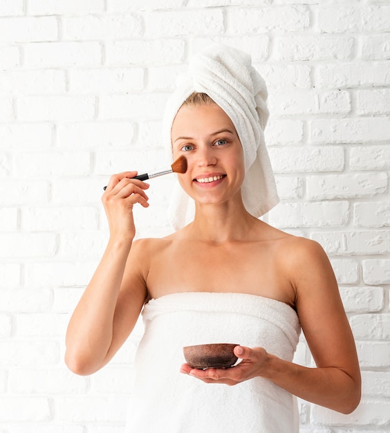 Young beautiful woman wearing white towels applying scrub on her face