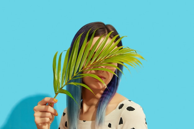 Young beautiful woman with blue hair holding palm leaf 