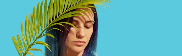 Young beautiful woman with blue hair holding palm leaf 