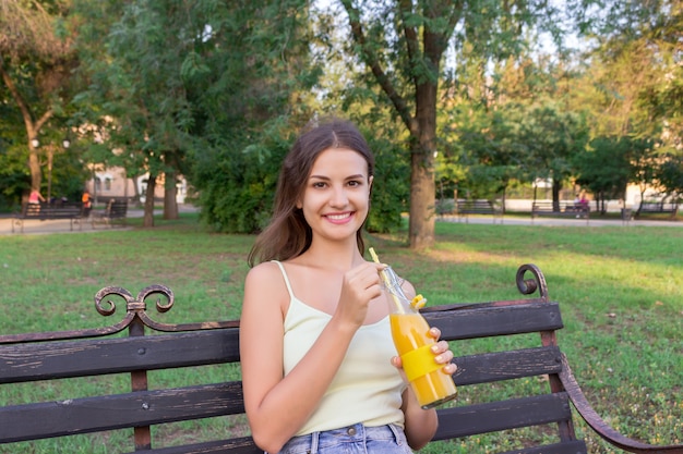 Young beautiful woman with a bottle of fresh orange juice enjoys a great weather in the park