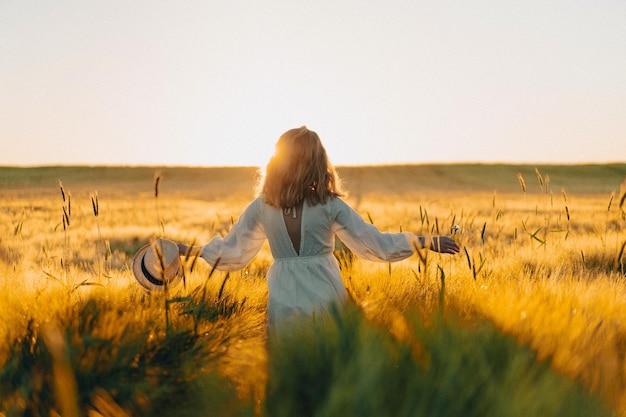 young beautiful woman with long blond hair in a white dress on a wheat field in the early morning at sunrise. Summer is the time for dreamers, flying hair, a woman running across the field in the rays