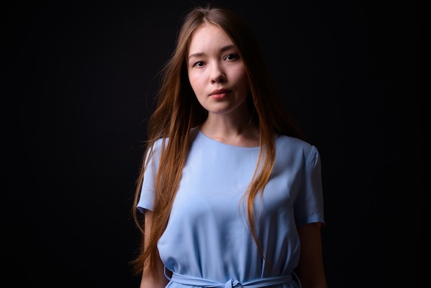 Young beautiful woman with long brown hair against black wall