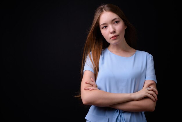 Young beautiful woman with long brown hair against black wall