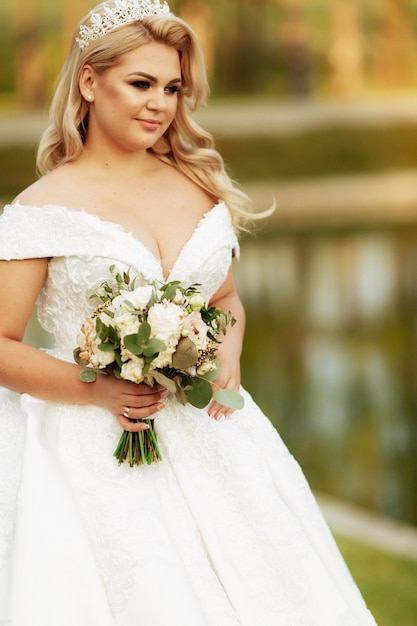 Young beautiful woman with long hair and blue eyes in long fabulous wedding dress in autumn park. Fairytale princess in the fall wood.