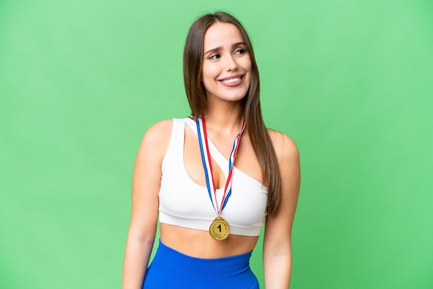 Young beautiful woman with medals over isolated chroma key background looking up while smiling