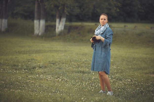 Young beautiful woman with red hair and a denim dress standing on the lawn in the Park