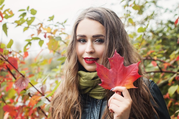 Young beautiful woman with red maple autumn leaf outdoors