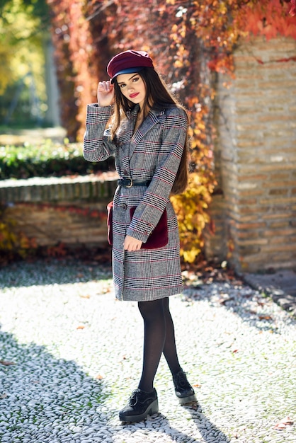 Young beautiful woman with very long hair wearing winter coat and cap in autumn leaves background