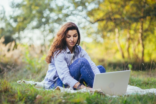 Young beautiful  woman working on a laptop sitting on the grass