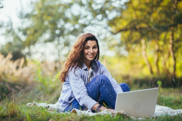 Young beautiful  woman working on a laptop sitting on the grass