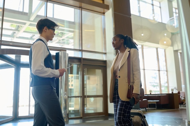 Young bellboy in uniform meeting black woman in smart casualwear in lounge