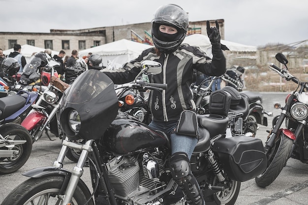 Photo a young biker womanrocker woman in a motorcycle helmet sitting on a motorcycle and shows a goat gesture or a rock symbola hand gesturecoolpartyrespectthe concept of victory and coolness