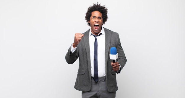 Young black afro man shouting aggressively with an angry expression or with fists clenched celebrating success