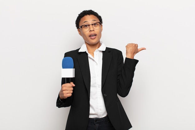 Young black afro woman looking astonished in disbelief, pointing at object on the side and saying wow, unbelievable