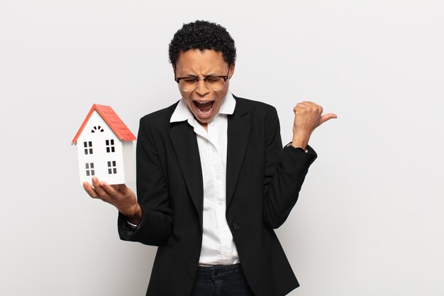 Young black afro woman shouting aggressively, looking very angry, frustrated, outraged or annoyed, screaming no