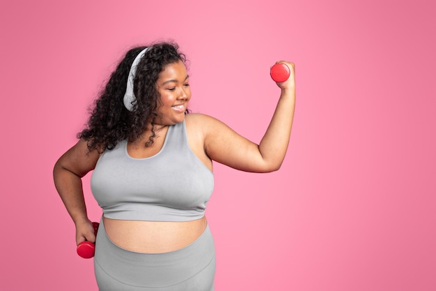 Young black body positive lady in sportswear and wireless headphones doing exercise with hand