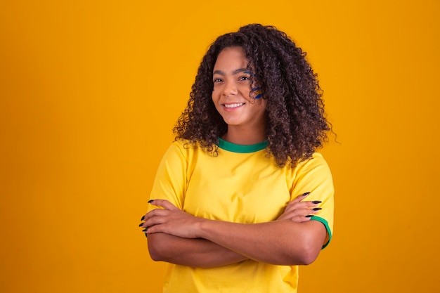 Young black Brazilian soccer fan arms crossed over the body Beautiful brazilian cheerleader with arms crossed on yellow background