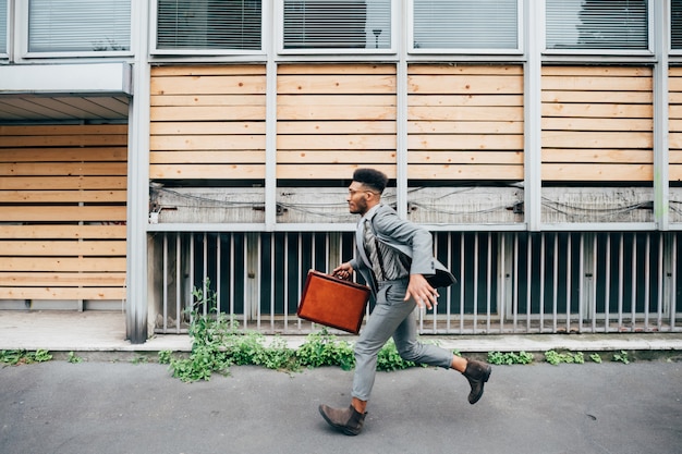 Young black businessman holding briefcase running outdoor