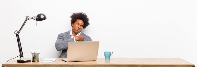 Young black businessman looking arrogant, successful, positive and proud, pointing to self on a desk