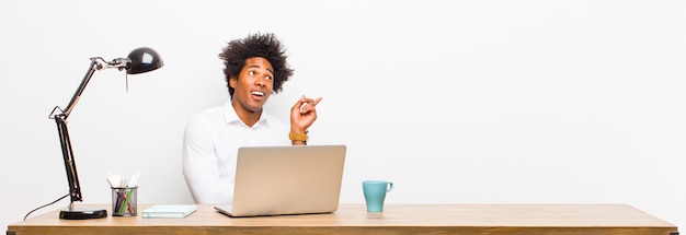 Young black businessman smiling happily and looking sideways, wondering, thinking or having an idea on a desk