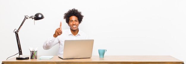 Young black businessman smiling and looking friendly, showing number one or first with hand forward, counting down on a desk