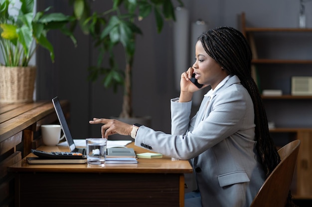 Young black businesswoman at office desk calling business partner to talk about project details