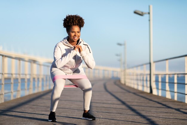 Young Black Female In Sportswear Training With Resistance Loop Band Outdoors