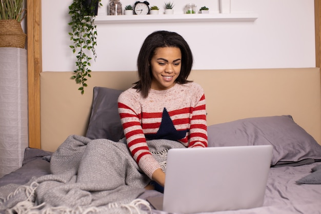 Young black girl with laptop computer, sitting in bright living room.