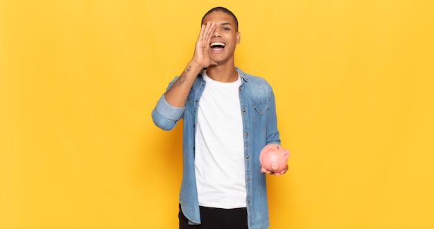 Young black man feeling happy, excited and positive, giving a big shout out with hands next to mouth, calling out