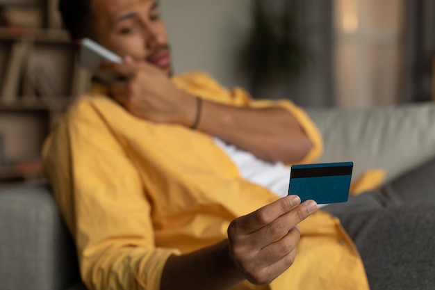 Young black man holding credit card calling to bank client service having problem during online shopping at home