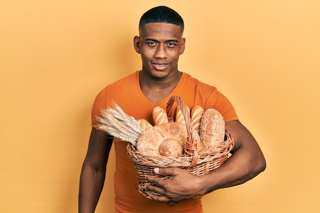 Young black man holding wicker basket with bread looking positive and happy standing and smiling with a confident smile showing teeth